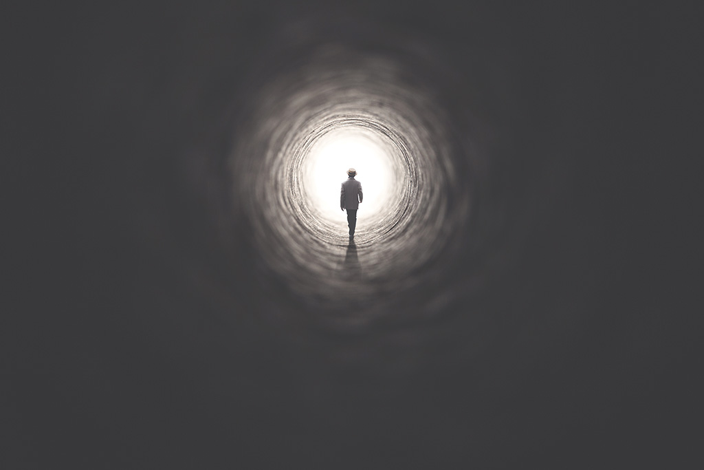 Silhouette of man in tunnel with light at the end representing life after death